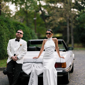 Couple in formal attire leaning on convertible car.