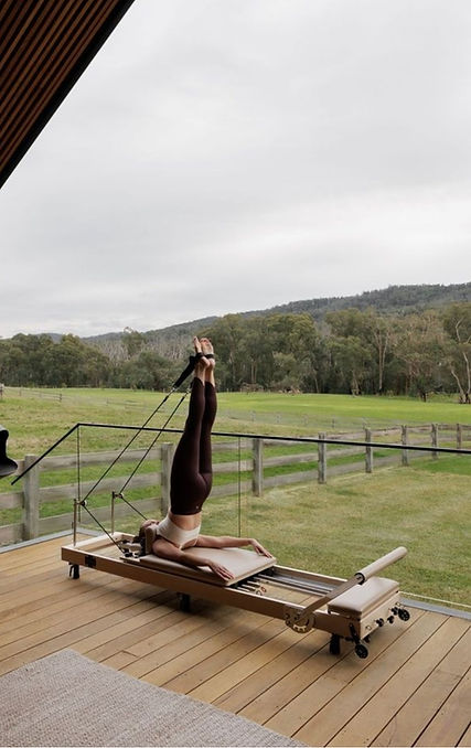 Woman on pilates reformer on a deck with nature backdrop