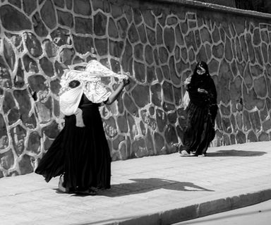 Deux femmes en habit traditionnel marchent le long d'un mur de pierre. Atlas Maroc