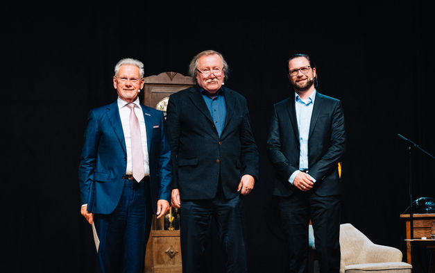 Der Moderator, der Referent und Dr. Manfred Wittenstein stehen auf der Bühne