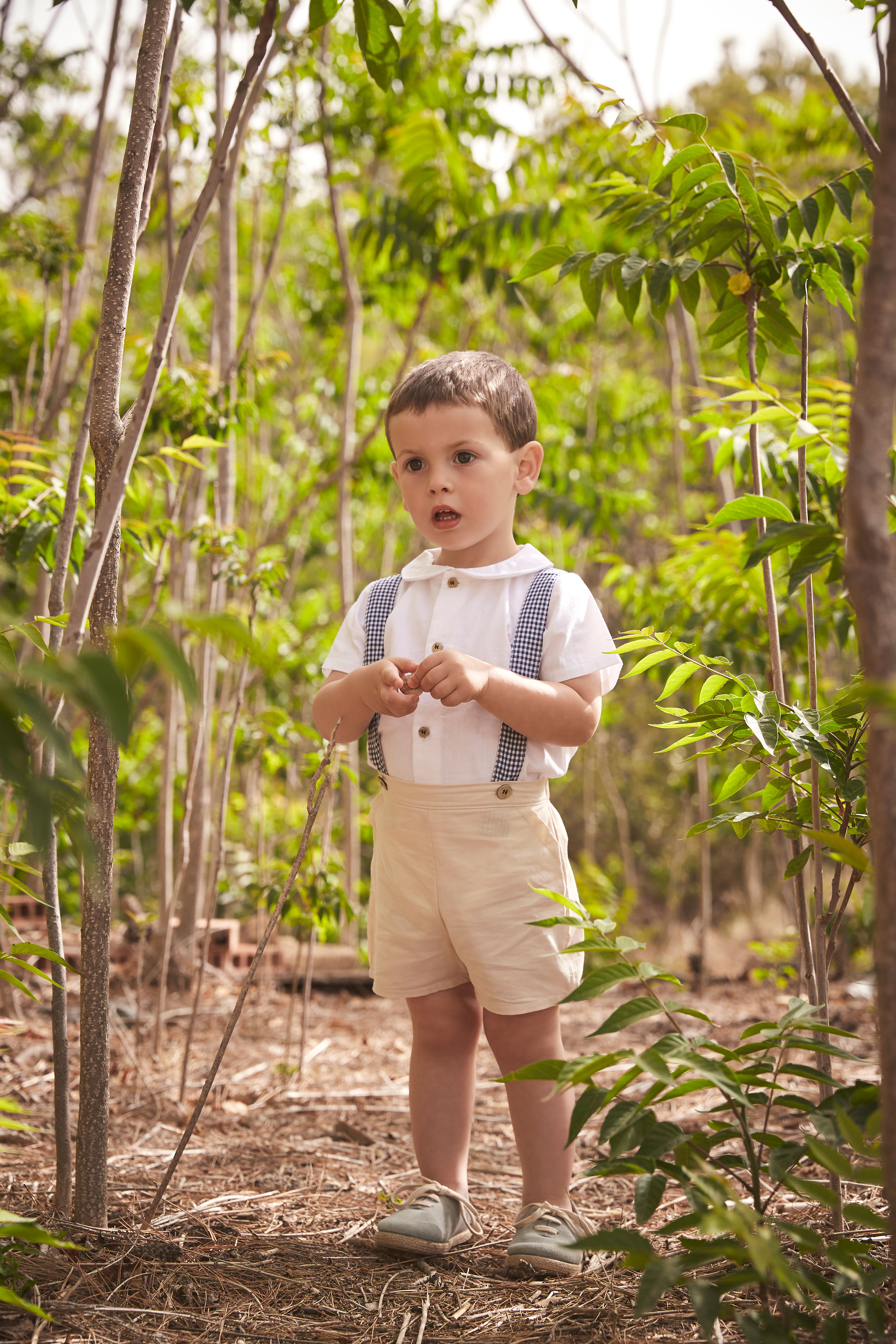 Babidu boys sandy beige shorts paired with a creamy white perter pan collar shirt and navy gingham brace straps
