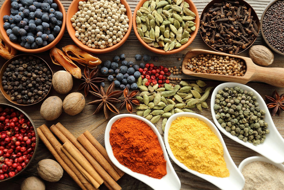 Variety of colorful spices in wooden bowls on a brown wooden surface.