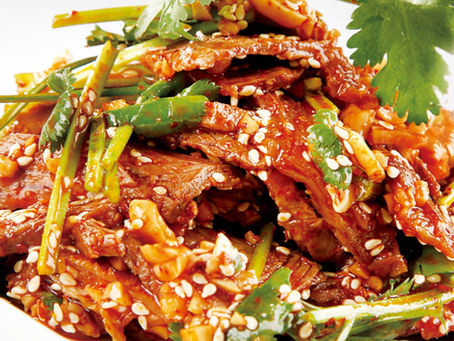 Close-up of a spicy Chinese dish with sesame seeds and herbs.
