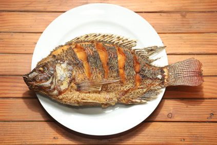 Fried whole fish on white plate, wooden table background, delicious meal.
