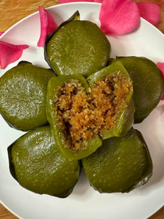 盘子里诱人的绿色粿，切开的粿展示着馅料，周围散落着粉色花瓣。