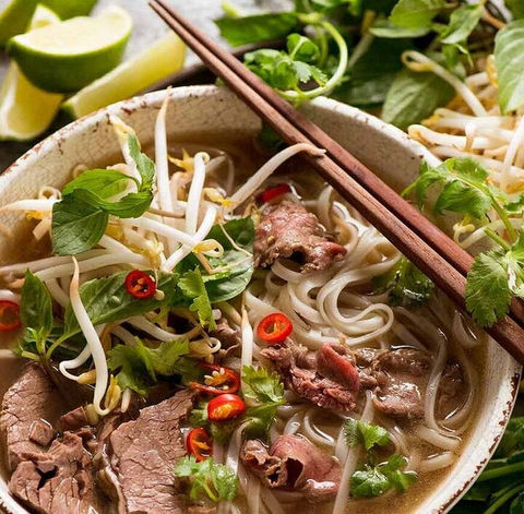Bowl of delicious Vietnamese pho with chopsticks and fresh ingredients.