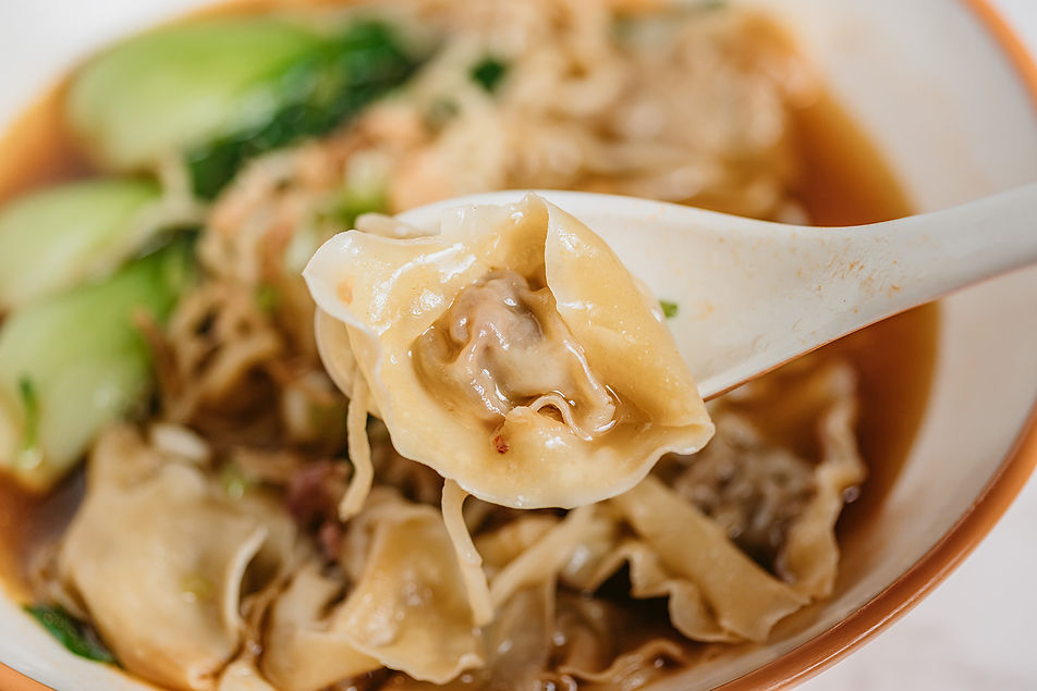 Close-up of a dumpling on a spoon with noodles and soup.
