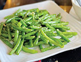 盘子里的炒豆角,呈绿色,看起来清新,在白色盘子上。