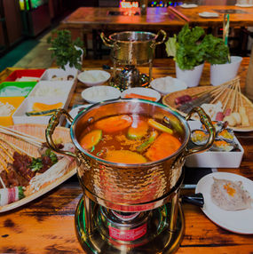 Hot pot with simmering broth, skewered ingredients, and vegetables