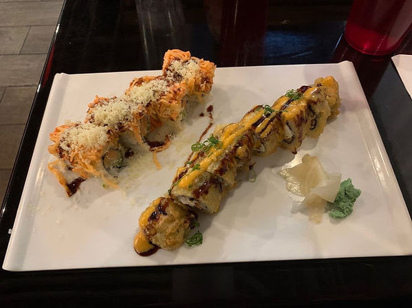 盘子里的两卷炸寿司,上面淋着酱汁,旁边有姜和芥末。