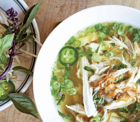 Bowl of chicken pho with toppings and a side of herbs