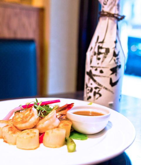 Grilled scallops and shrimp with a small sauce and sake bottle.