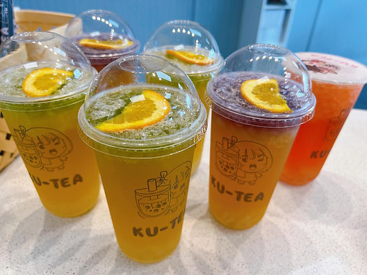 Various Ku-Tea drinks, iced with orange slices, on display in a cafe setting.