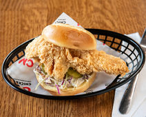 Chicken sandwich with coleslaw and pickles in a black basket, delicious meal.