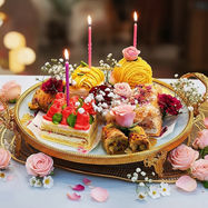 Elegant dessert tray with cake, pastries, lit candles, and pink roses.