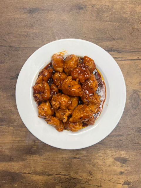 Plate of orange chicken on a white plate on wood background.