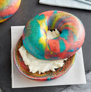 Rainbow bagel with cream cheese on parchment paper, delicious colorful breakfast.