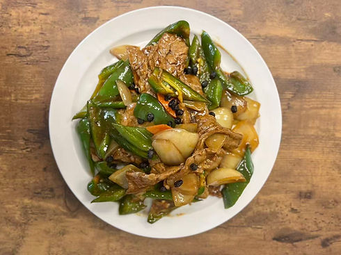 Beef and green peppers on a white plate, served on a wooden table.