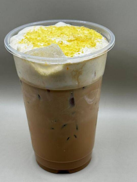 Iced coffee drink with creamy foam and yellow sprinkles in a plastic cup.