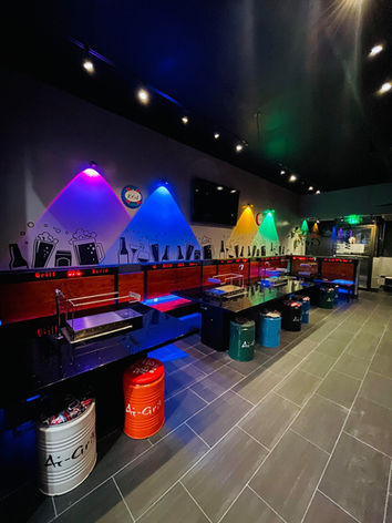Modern restaurant with colorful lighting, booth seating, Coca-Cola and Pepsi barrels.