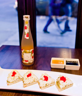 Sushi, bottle, and dipping sauce arranged on a table near a window.