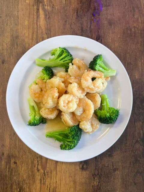 Shrimp with broccoli on a white plate, delicious meal, wooden table background.
