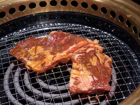 Two pieces of raw marinated beef cooking on a Korean BBQ grill.