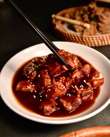 用筷子夹起红烧排骨,菜肴特写,美味排骨,棕色酱汁,美食摄影