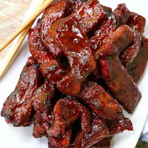 Glazed barbecued pork pieces on a white plate with chopsticks.