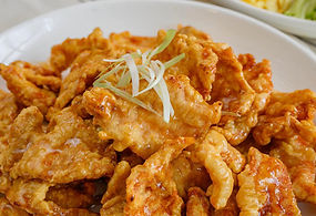 盘子里的炸鸡菜肴，配有葱丝，背景是蔬菜，美味可口。