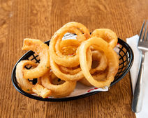 Golden crispy onion rings in a black basket on a wooden table.