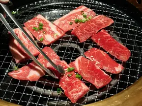 Tongs grilling sliced raw beef on a hot metal grate.
