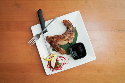 Grilled chicken served with sauce, lemon slice, fork, and knife on white plate.