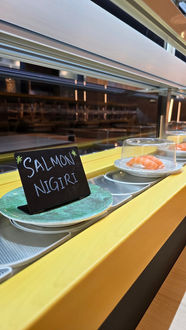 鲑鱼握寿司在旋转传送带上,上面写着“鲑鱼握寿司”,美食背景