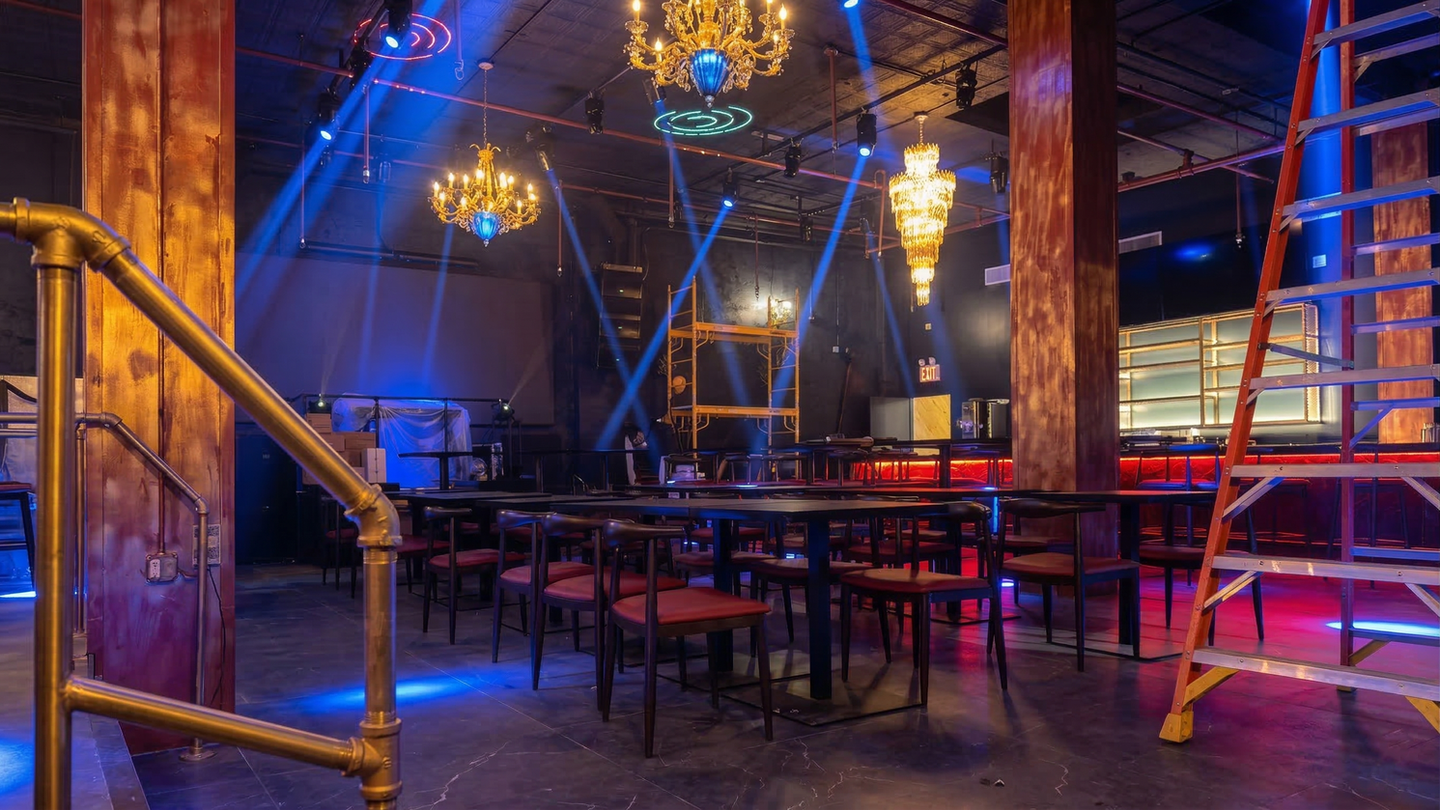 Elegant event venue with ornate chandeliers, blue spotlights, and empty tables.