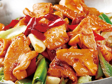 Close-up of stir-fried food with red peppers and green onions in bowl