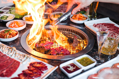 烧烤炉上的手用夹子夹着肉,火焰旺盛,周围摆放着小菜。