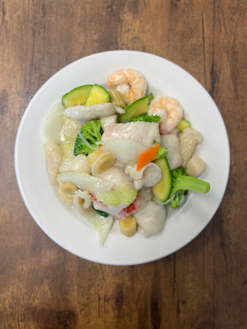 White plate of seafood dish with shrimp, fish, and vegetables.