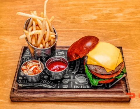 Cheeseburger with lettuce, tomato, fries, ketchup, and coleslaw on a wooden tray.