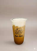 KU-TEA drink with foam on top, refreshing beverage in a transparent cup on table.