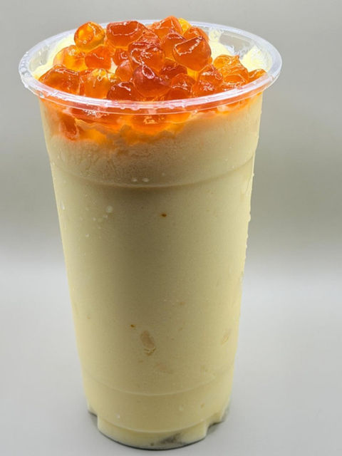 Creamy mango shake in a plastic cup with orange popping boba.