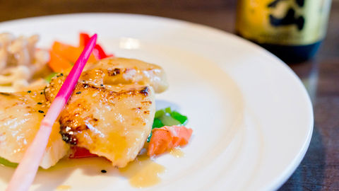Grilled scallop on white plate with vegetables and a bottle of soy sauce.
