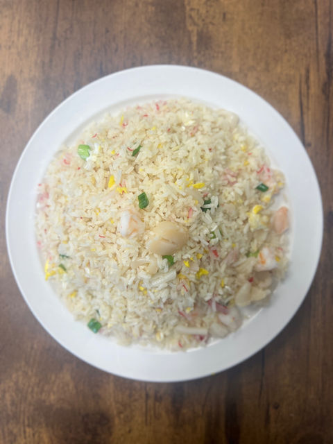 Plate of seafood fried rice on a wooden table, top view.