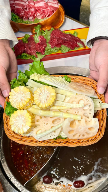 Hands holding basket of corn, lotus root, bamboo, lettuce for hotpot.