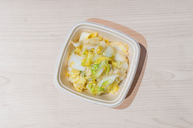 Cooked Napa cabbage in a white takeout container on a wooden table.