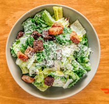 Caesar salad in grey bowl with croutons and cheese on wood surface.