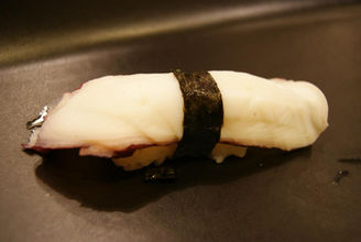 章鱼寿司,上面有海苔,放在黑色盘子里,这是一道日式美食。