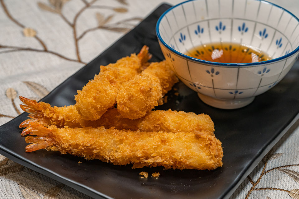 Golden fried shrimp tempura on black plate with dipping sauce.