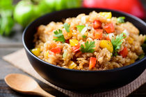 Bowl of rice with peppers and cilantro, on a wooden table.