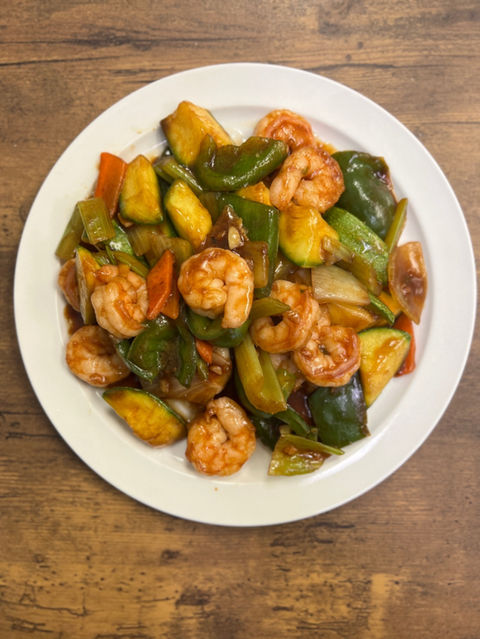 Shrimp stir-fry dish with vegetables on white plate, wooden table.